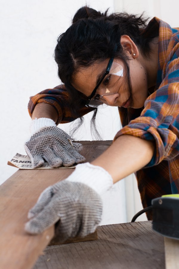 Woman with goggles sanding a piece of wood