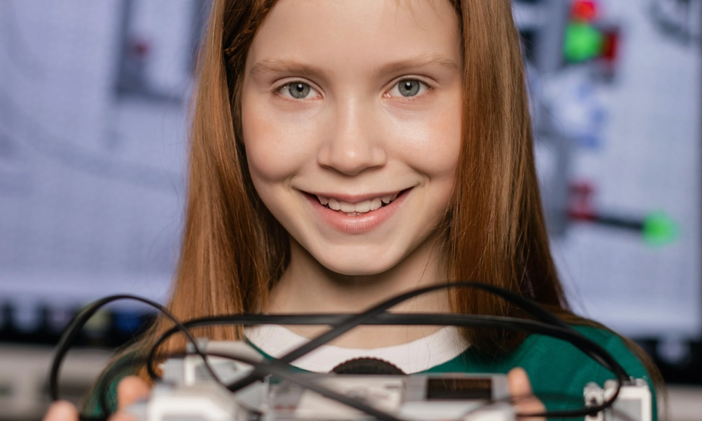 Primary school student smiling and holding a car built out of building blocks and wires in her hands