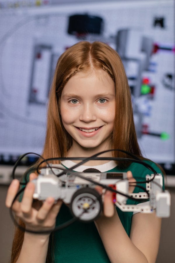 Primary school student smiling and holding a car built out of building blocks and wires in her hands