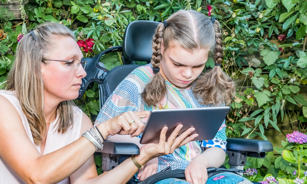 Person showing tablet to a child in a wheelchair