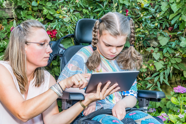 Person showing tablet to a child in a wheelchair
