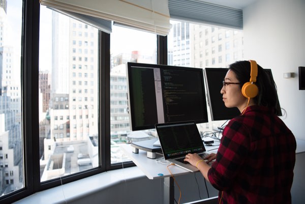 Software engineer writing code on a computer in front of a city setting with skyscrapers