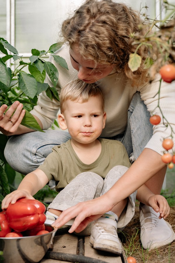 A woman is sitting with her son with fresh vegetables around them