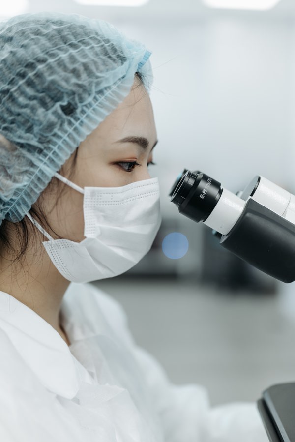 Person with a mask looking through the microscope