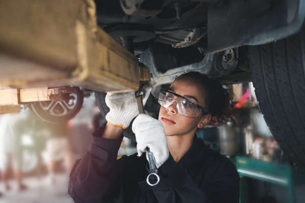 Person with work safety glasses and a tool is inspecting a vehicle from underneath
