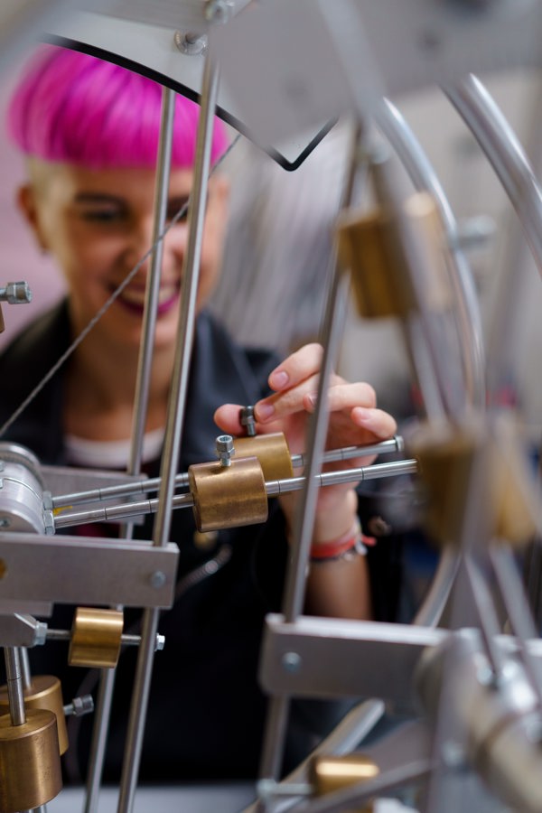 Person with pink hair is turning a screw on a wheel