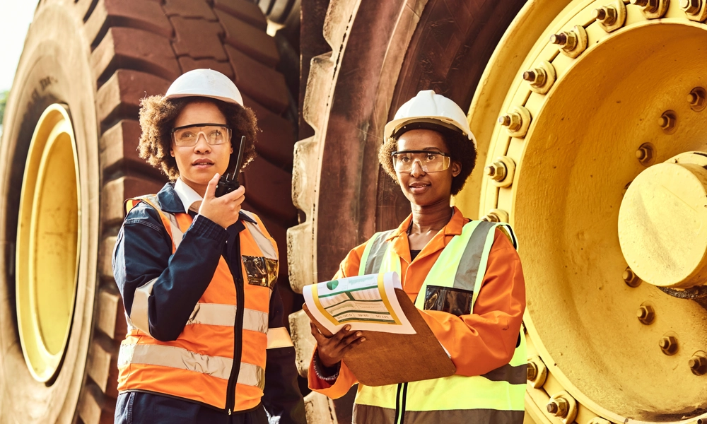 Two people standing with hard hats in front of a mining truck