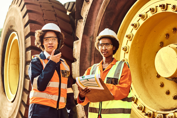 Two people standing with hard hats in front of a mining truck