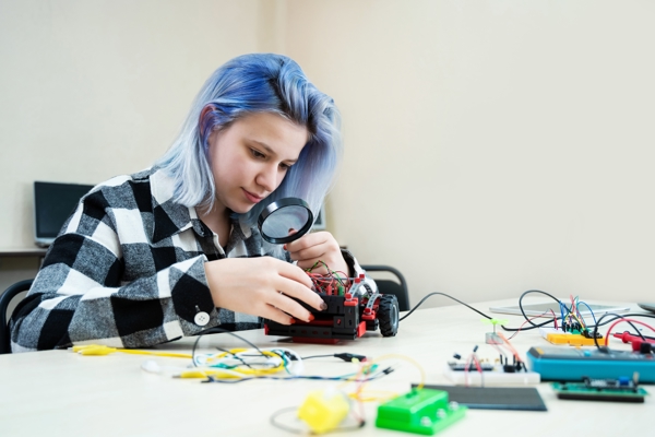 Student looking at a circuit of a toy car with a magnifying glass