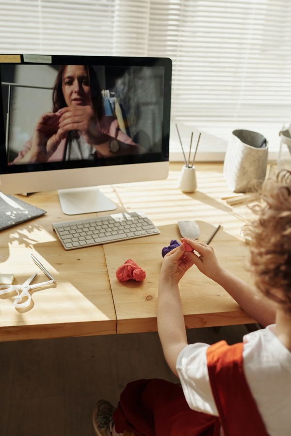Teacher on the monitor showing a student at home how to shape a dough