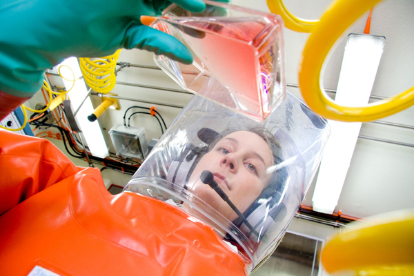 Person in a bio-hazard suit checking out a liquid in a container