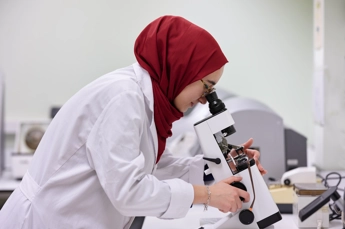 Person wearing a laboratory coat is looking at glasses through a microscope