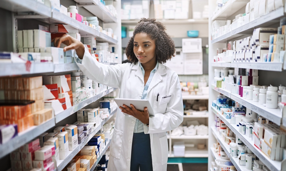 Person with a white coat is holding a notepad and looking at medications on the shelves
