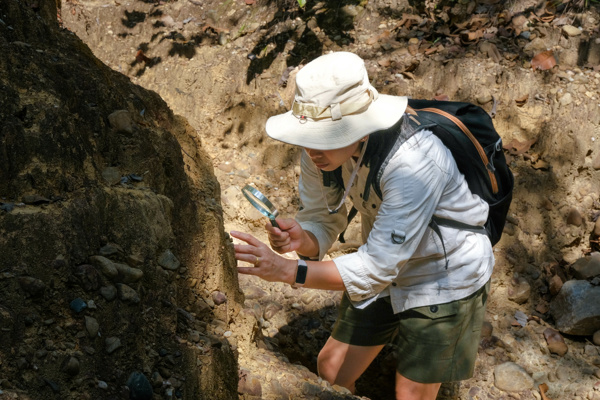 Woman with a magnifying glass is looking at the rocks