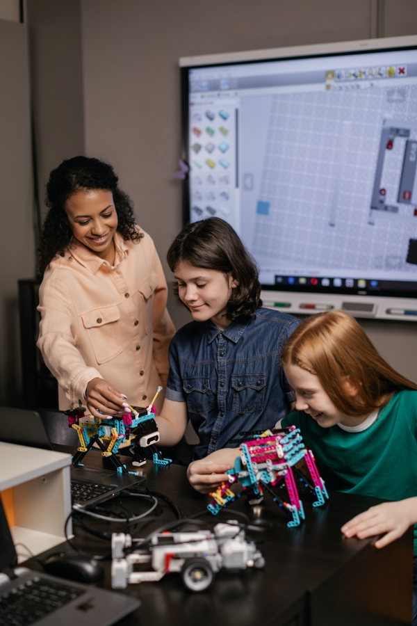 Teacher looking at STEM gadgets made out of building blocks with two secondary school aged students in a classroom