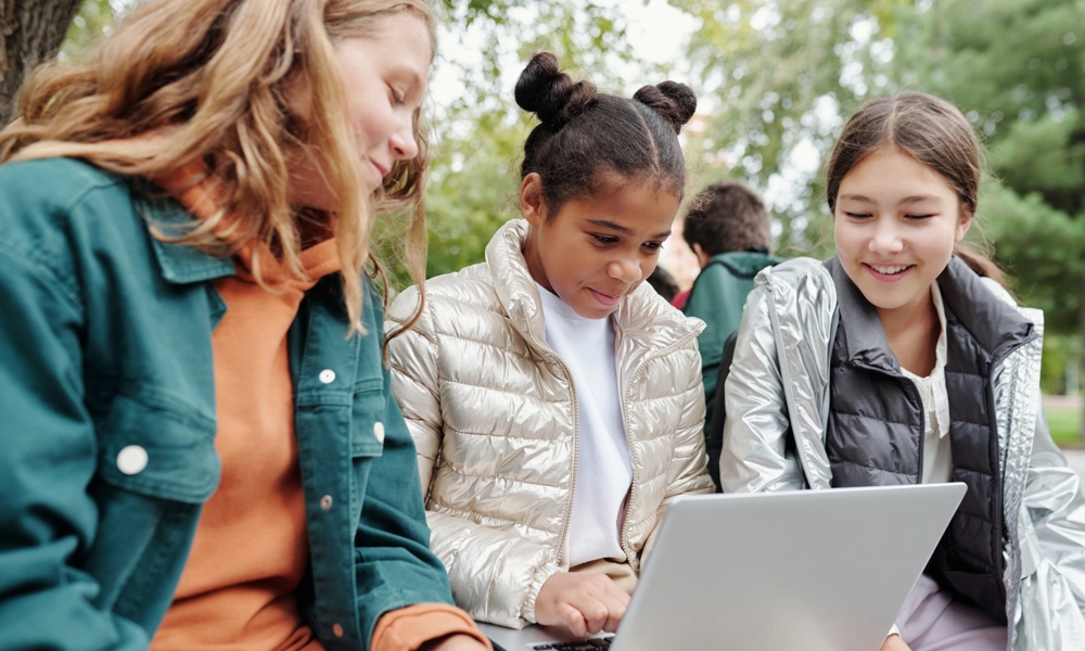 Three students sitting outdoor and looking at a laptop