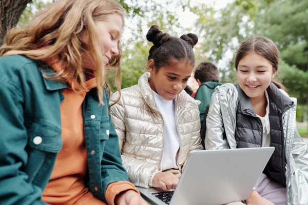 Three students sitting outdoor and looking at a laptop