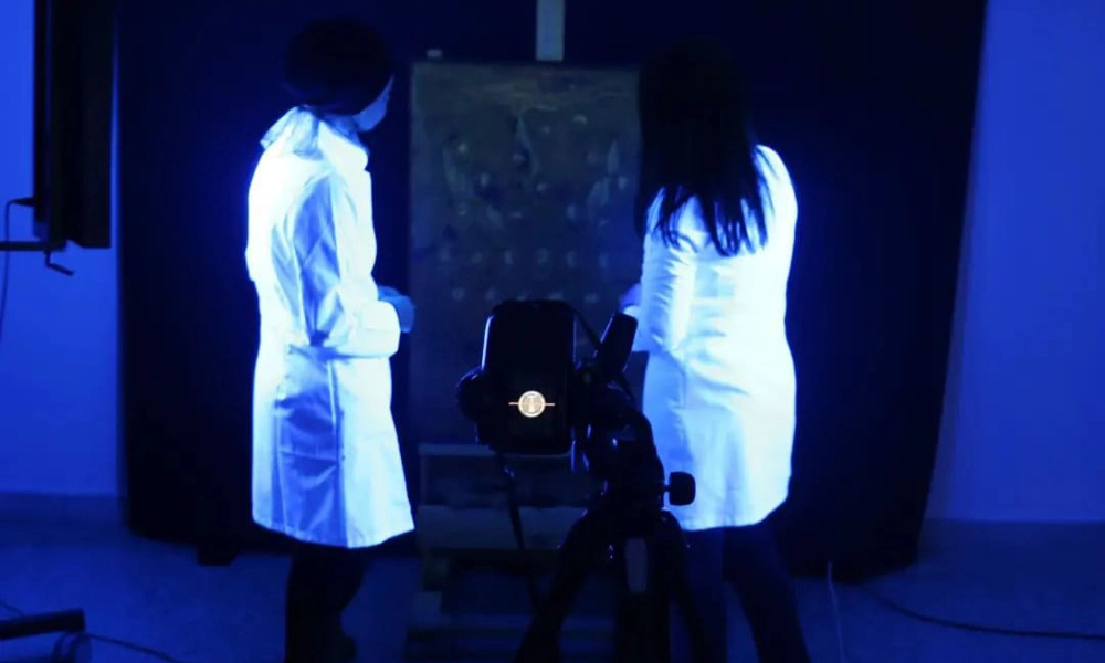 Two people in laboratory coats looking at a painting in UV light