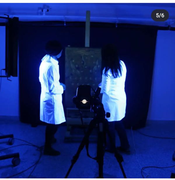 Two people in laboratory coats looking at a painting in UV light