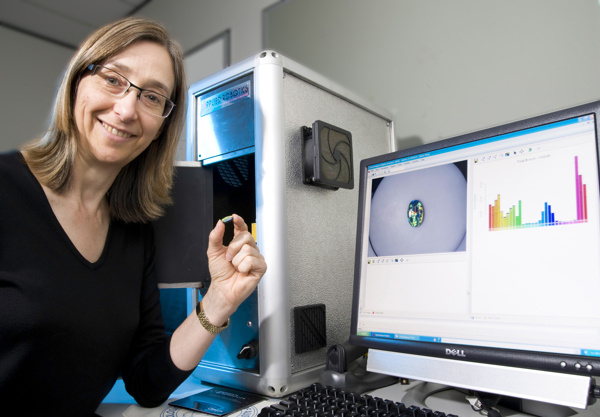 Person holding a pill next to a computer screen showing graphs