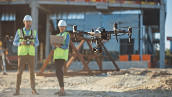 Two people with hard hats flying a drone in a construction site