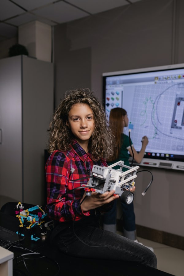 Student holding a robot toy while another student is drawing on the board