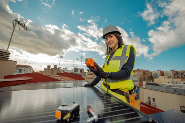 Person with a hard hat and high-vis wear is on the roof working on solar panels