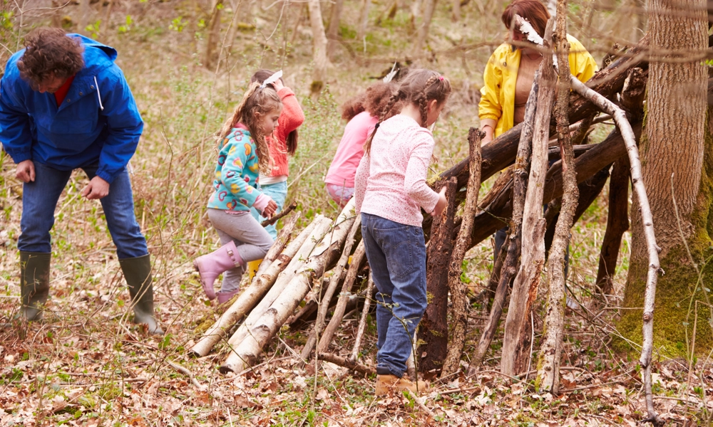 A group of children and two adults are making a shelter from tree branches