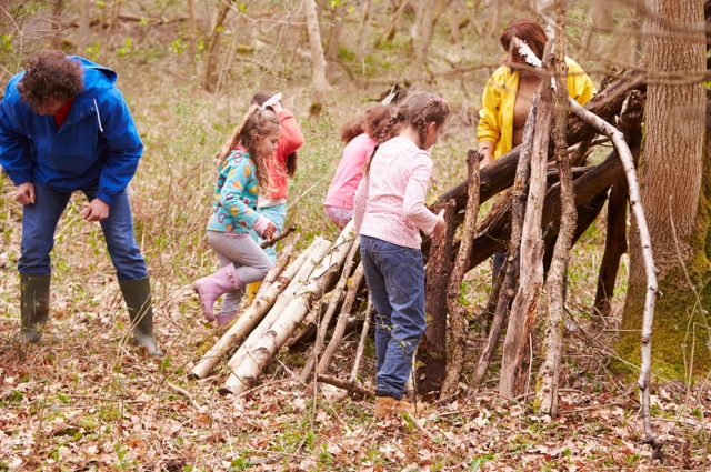 A group of children and two adults are making a shelter from tree branches