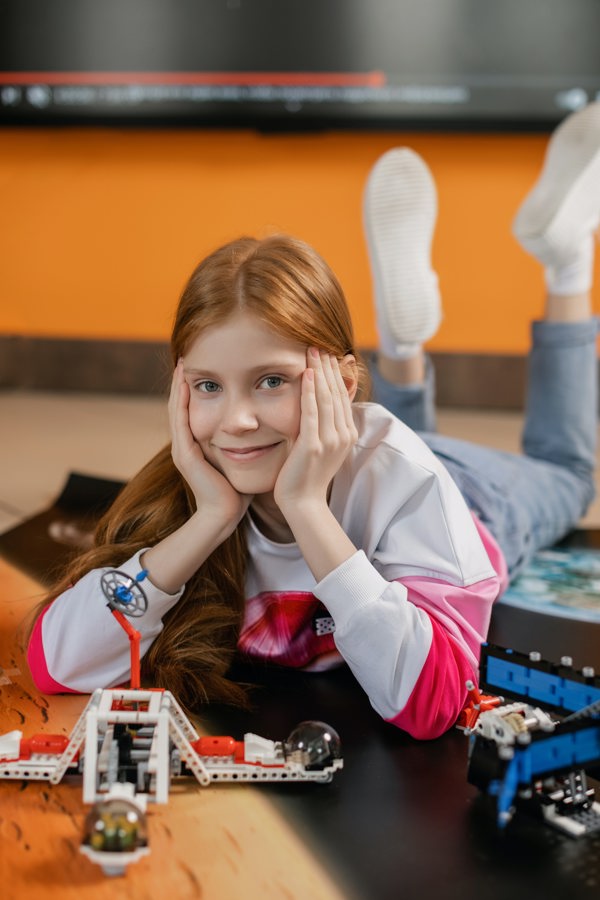 Primary school student smiling and holding a car built out of building blocks and wires in her hands