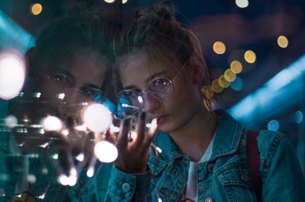 Young woman and her reflection in a window with atmospheric lights