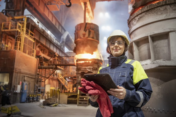 Worker in a hard hat is posing in front of a metal furnace