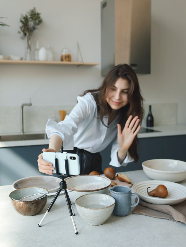 Person waving at her mobile phone set-up to show her and her kitchen