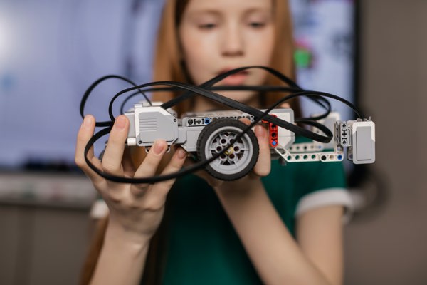 Primary school student smiling and holding a car built out of building blocks and wires in her hands