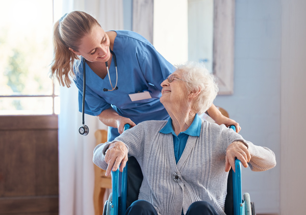 Person with a stethoscope around her neck is pushing an elderly person in a wheelchair